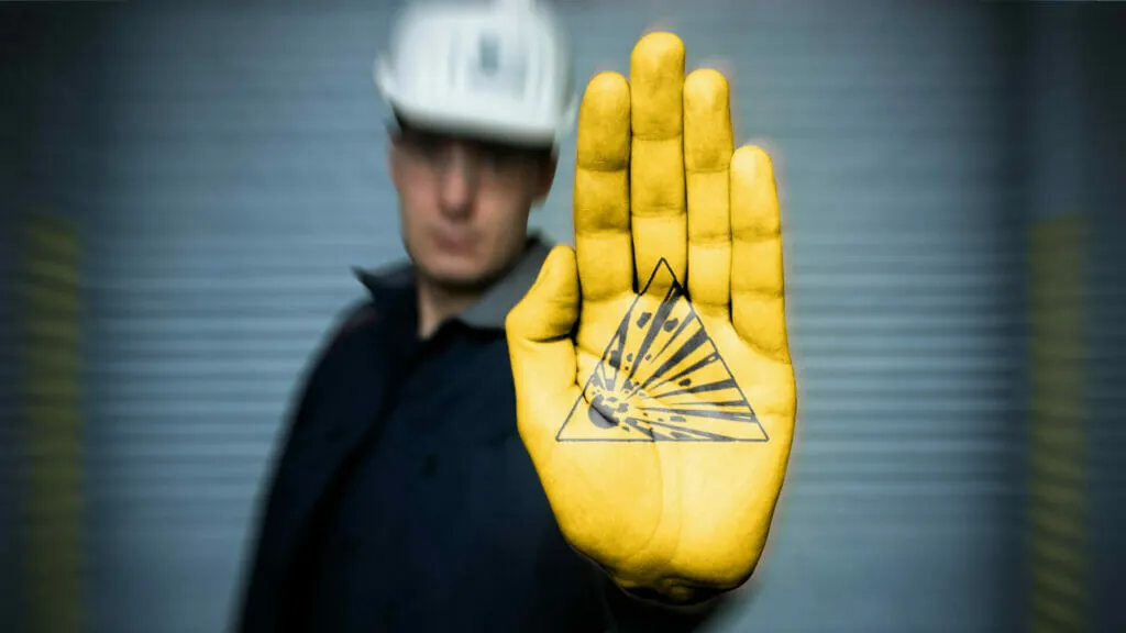 Sachverständiger für Explosionsschutz mit Helm und Overall, gelb bemalte Hand mit aufgemaltem W002 Symbol für Warnung vor explosionsgefährlichen Stoffen