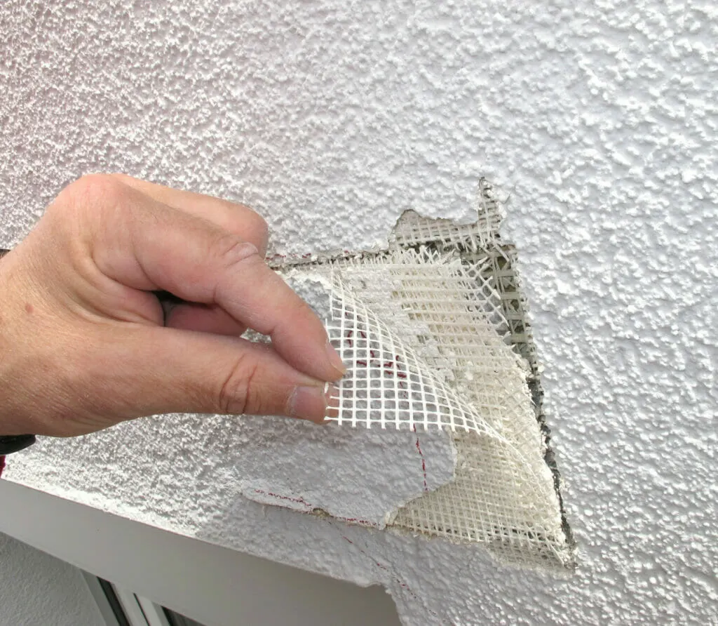 Sachverständiger für Putz- und Trockenbau inspiziert einen Putzschaden an einer Wand im Haus