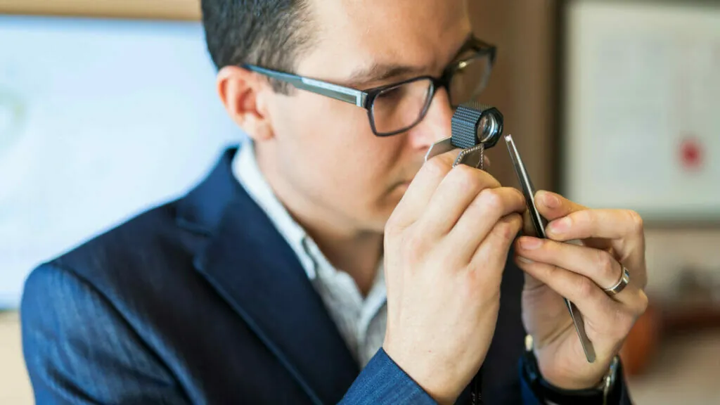 Sachverständiger für Wertgegenstände prüft mit einer Lupe einen Diamanten auf Echtheit