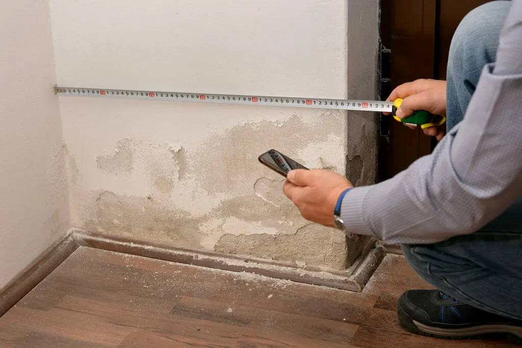 Wasserschaden Gutachter dokumentiert einen Feuchteschaden an der Wand mit Smartphone und Maßband