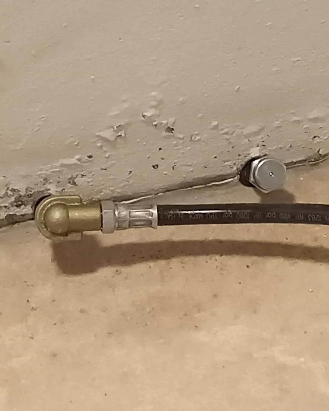 Injektionspacker an der Fuge zwischen Kellerwand und Boden, daran ein Hochdruckschlauch mit Messingkupplung