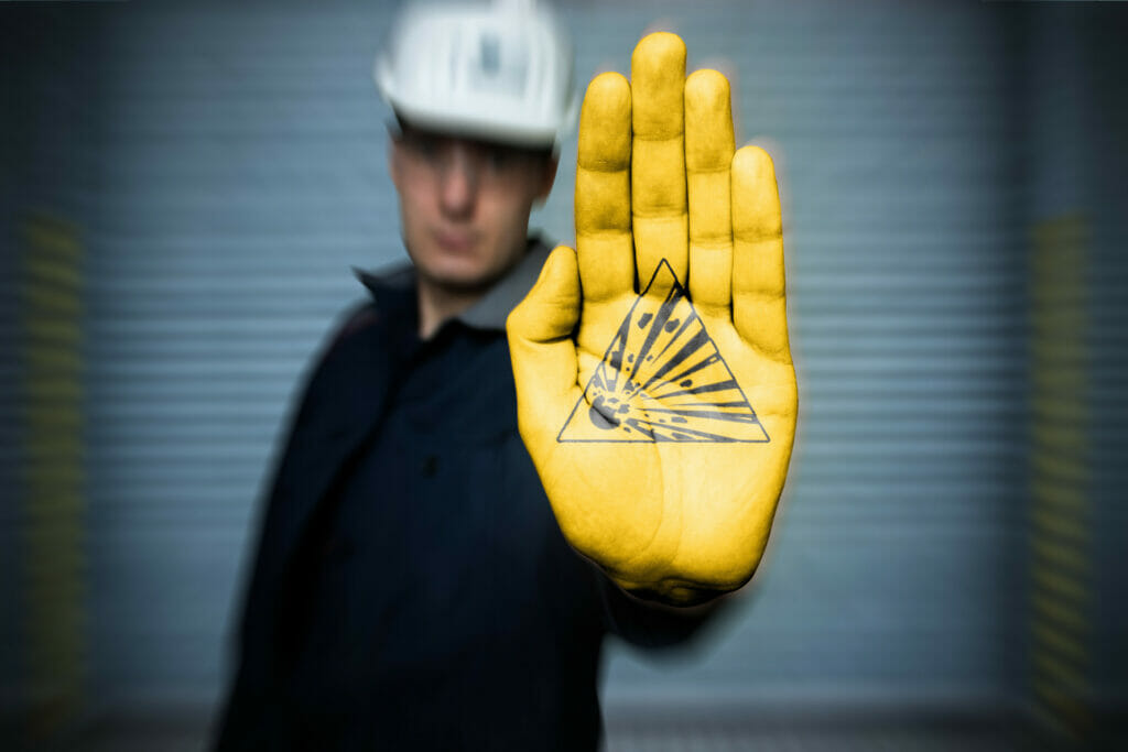 Sachverstaendiger fuer Explosionsschutz mit Helm und Overall gelb bemalte Hand mit aufgemaltem W002 Symbol fuer Warnung vor explosionsgefaehrlichen Stoffen